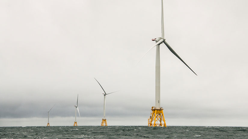A row of offshore wind turbines lined up in the ocean.