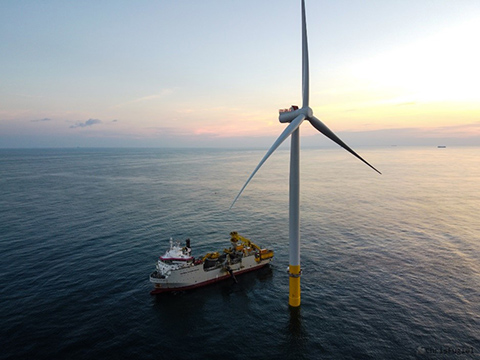 A vessel floats beside an offshore wind turbine.
