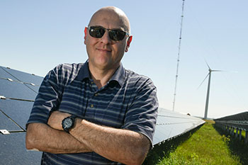 Vahan Gevorgian in sunglasses standing in front of solar photovoltaic panels and a wind turbine.