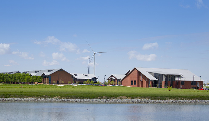 A wind turbine standing next to a school and lake.