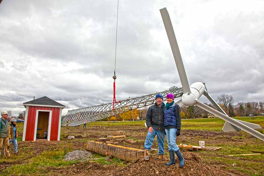 A couple stand in front of a wind turbine being erected by crane