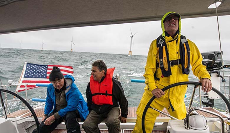 Three people on a boat drive away from offshore wind turbines.