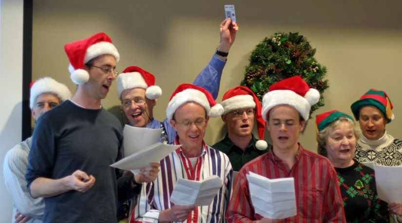 Eight people in Santa or elf hats singing.