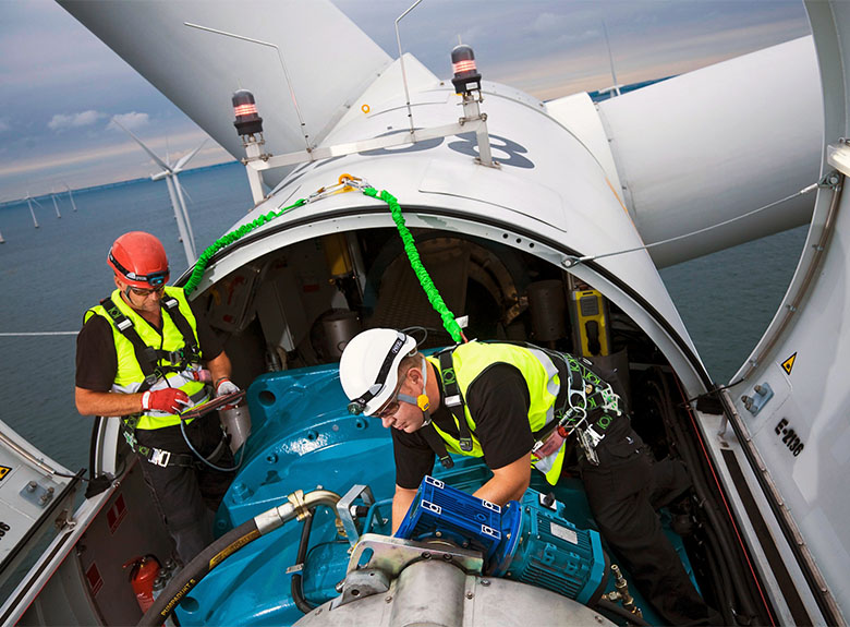 Workers in protective gear and harnesses work in the nacelle of an offshore wind turbine