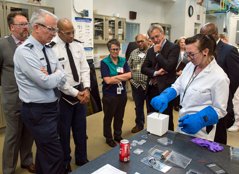 A group of people watch a scientist manipulate an object in the lab.