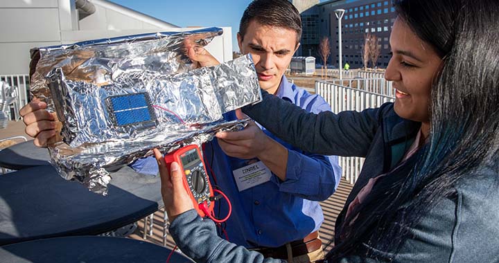 A man and woman work outdoors on a mini-solar concentrator.