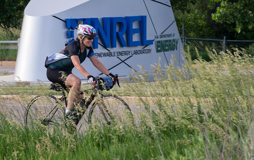 A woman riding her bike past the NREL entrance sign.