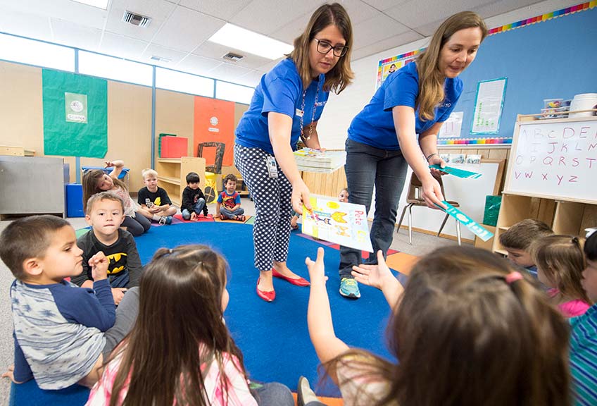 Two female NREL staff members hand out books to children in a classroom.