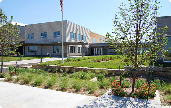 Photo of a new school building behind a flag pole and trees.