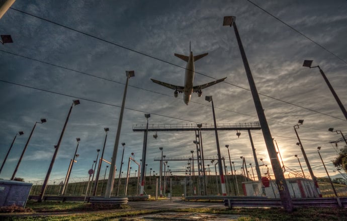 Photo of a large commercial airplane flying over electric infrastructure at an airport