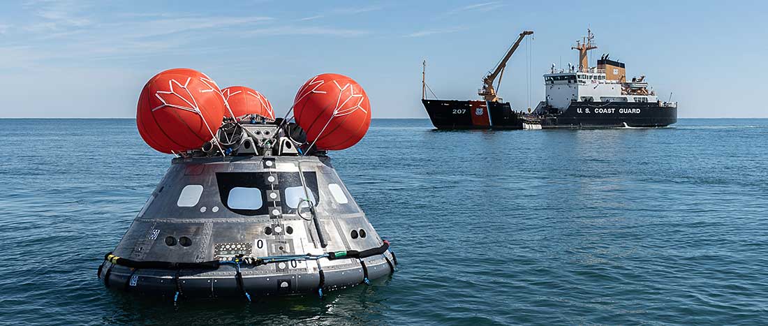 The spacecraft is right-side up as a U.S. Coast Guard boat floats behind it.