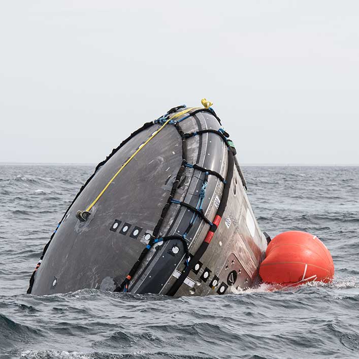 Closeup of the spacecraft that is almost upside down in the water.