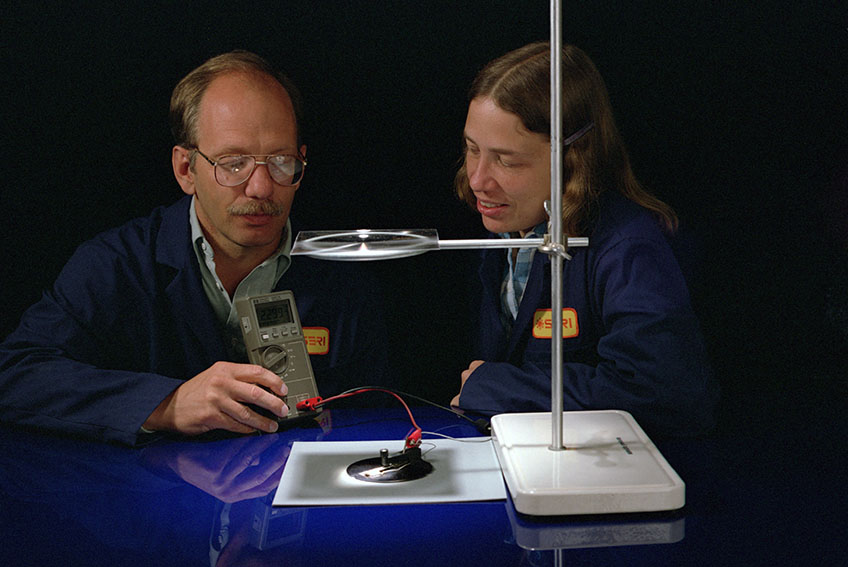 Two researchers hold a device to measure electrical output of a solar cell.