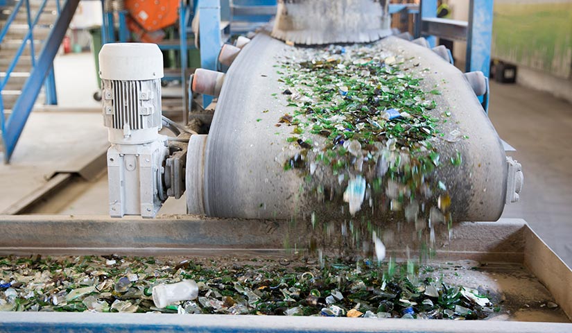 Photo of old broken glass of many shapes and sizes moving along a conveyer belt at a glass recycling center.