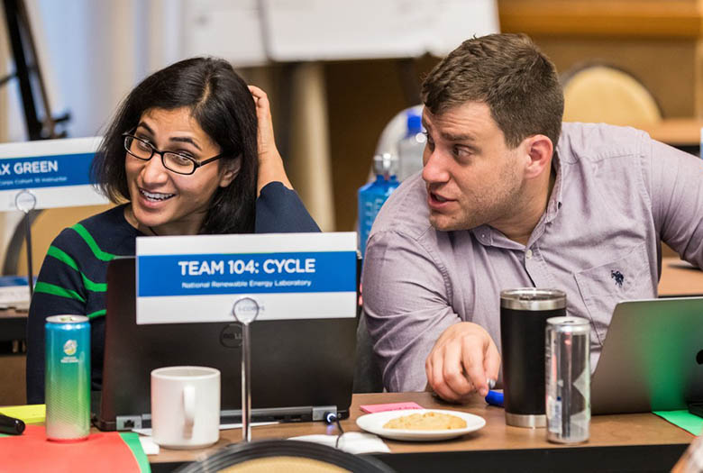 Avantika Singh and Nic Rorrer sit and chat at a table behind a sign that reads: "Team 104: Cycle"