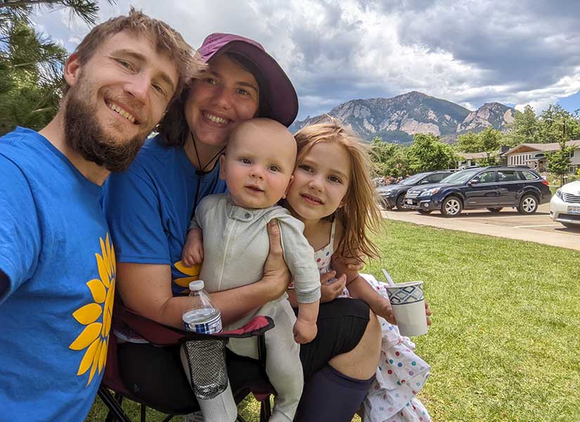 Andriy taking a selfie with a woman, a young girl, and a baby outdoors with mountain peaks in the background.