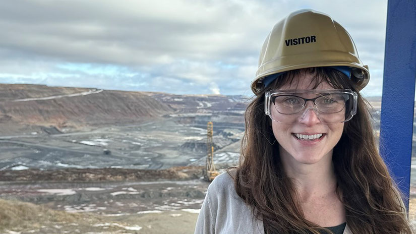 Kerry Rippy standing in front of a mining site wearing a hard hat and safety goggles