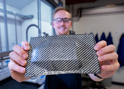 A researcher holds up a rectangle of carbon fiber composite.