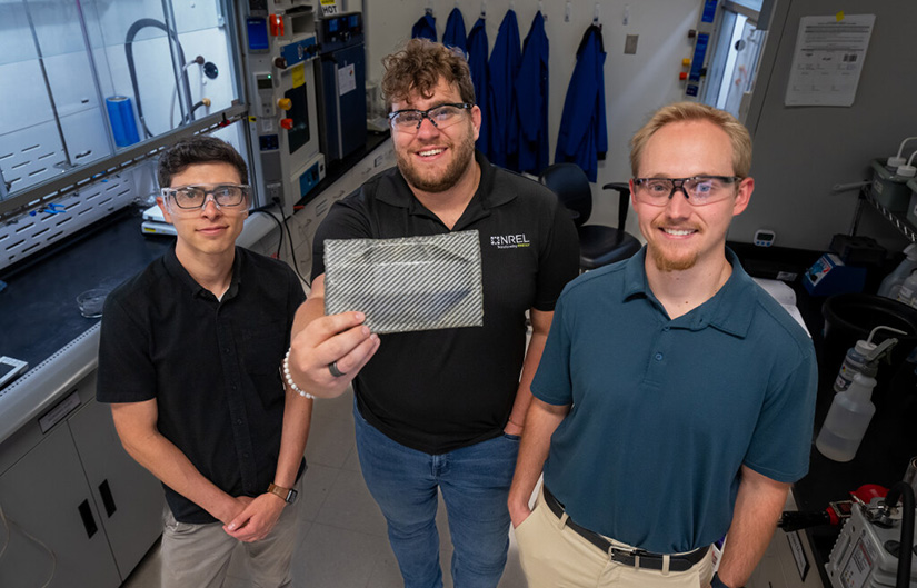 Three researchers in a lab hold up a recyclable carbon fiber composite sample.